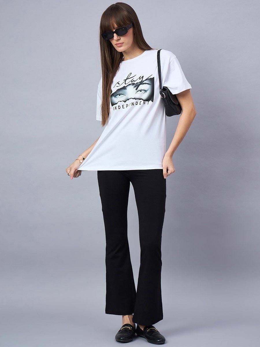 Woman in sunglasses wears a 98degreenorth Typography Print Drop Shoulder T-shirt with black flared pants and a shoulder bag.