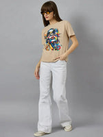 Woman in sunglasses wears 98degreenorth Typography Print Women’s Cotton T-shirt and white flared pants against gray background.
