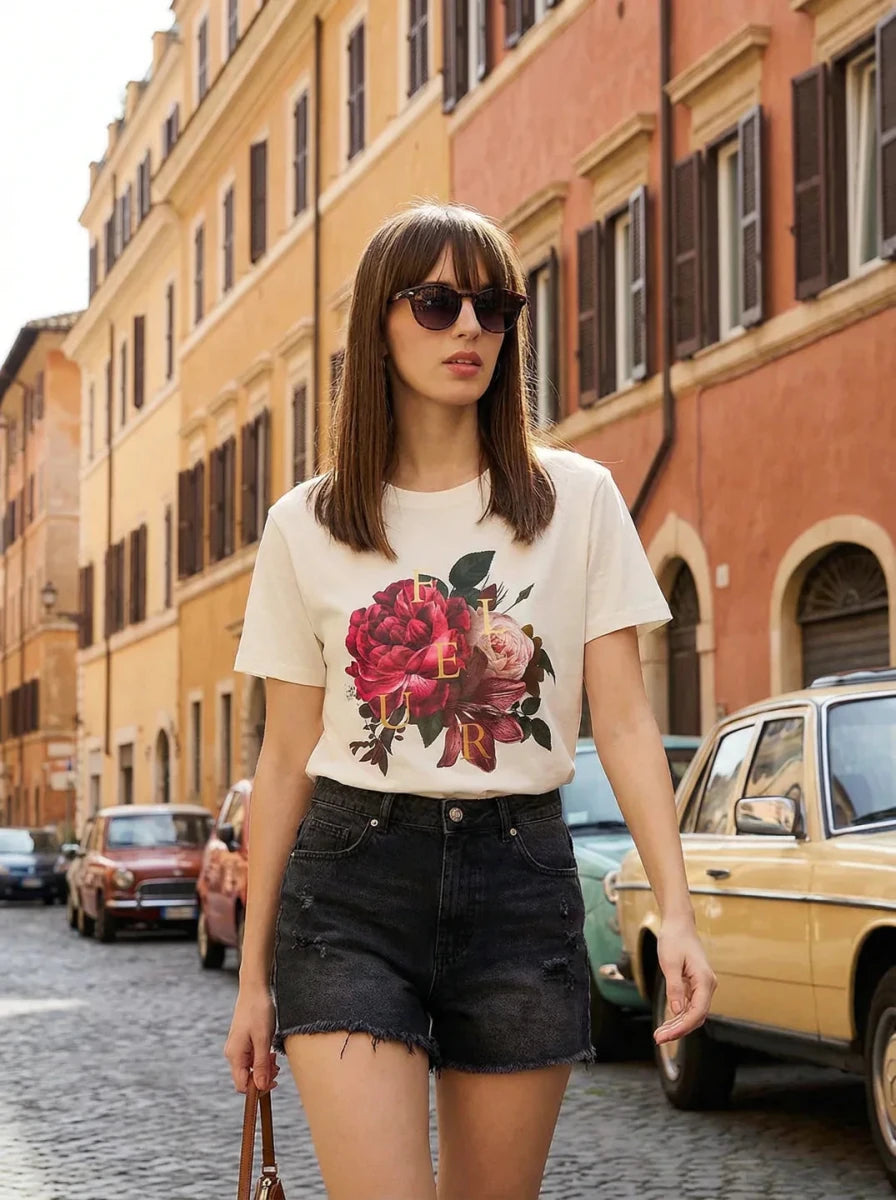 Woman in sunglasses wears a 98degreenorth Typography Printed Cotton Round Neck T-shirt, strolling along colorful buildings.