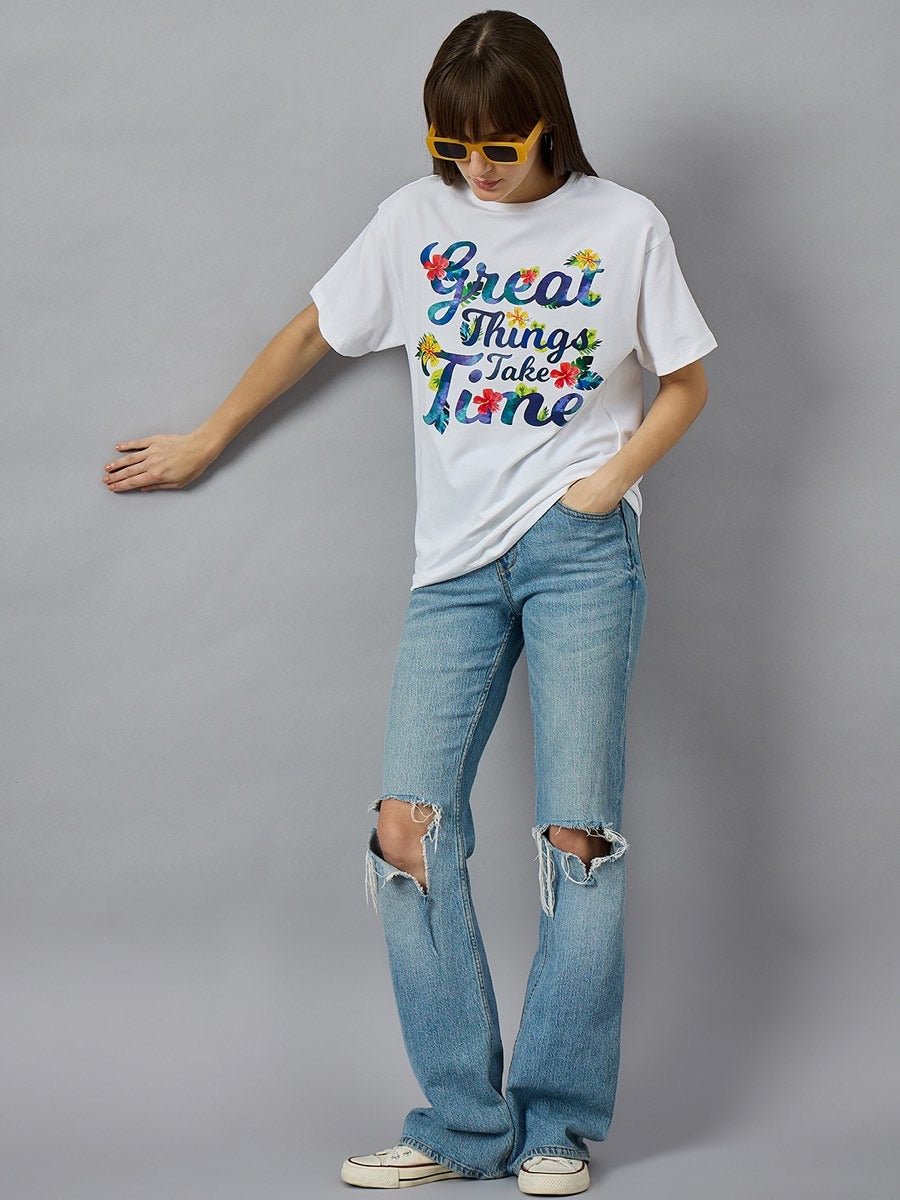 Woman in sunglasses and 98degreenorth Urban Streetwear Typography T-shirt, ripped jeans, poses by a gray wall.