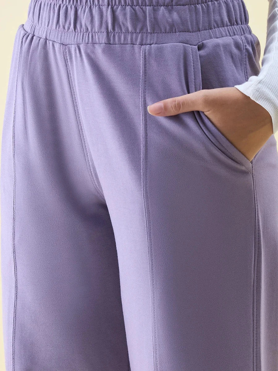 Close-up of a person in 98degreenorth Violet Wide Leg Pintuck Trackpants, hand in pocket, waist to mid-thigh.
