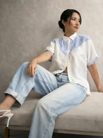 Woman in light blue jeans, white heels, and a 98degreenorth White Blue Colour Block Cotton Shirt sits on a bench.