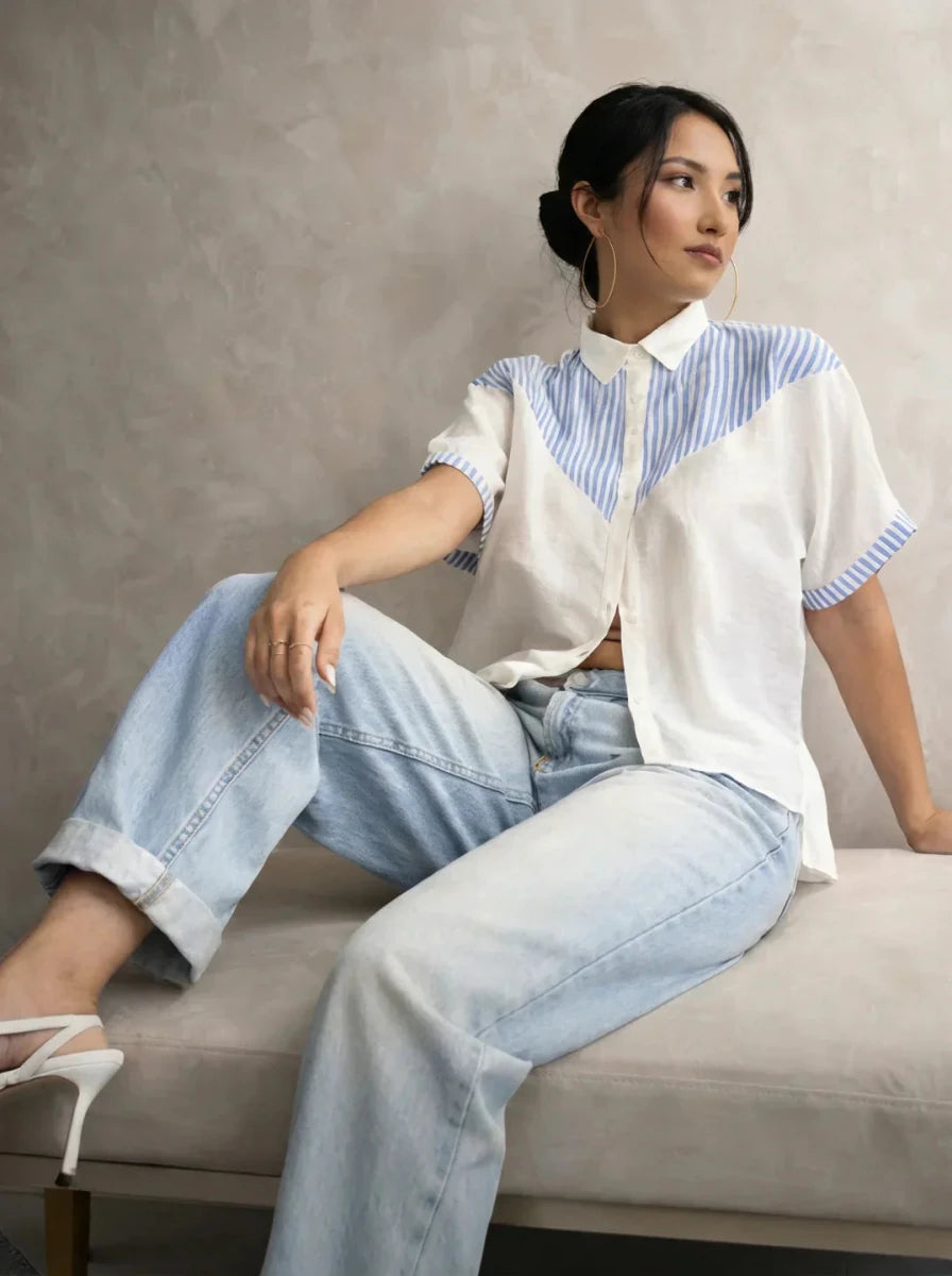 Woman in light blue jeans, white heels, and a 98degreenorth White Blue Colour Block Cotton Shirt sits on a bench.