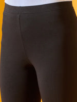 Close-up of a person wearing 98degreenorth Women Black Ankle-Length Leggings and a white top, shown from waist to mid-thigh against a solid yellow background.