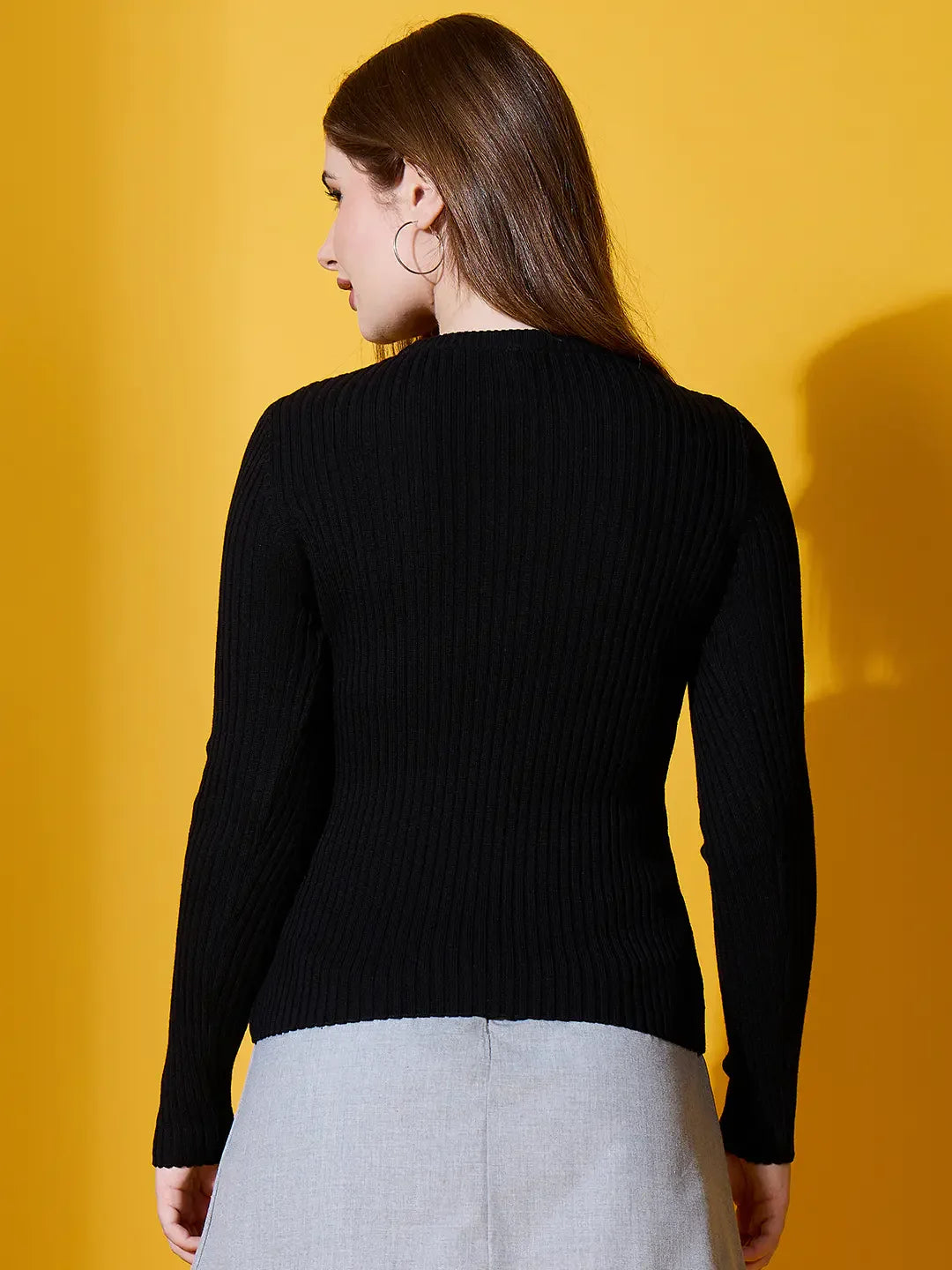 Woman wearing 98degreenorth Black Ribbed Round Neck Sweater, standing against a yellow background.
