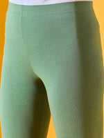 Close-up of a person in 98degreenorth Women Bright Green Ankle-Length Leggings and a white top, yellow background.