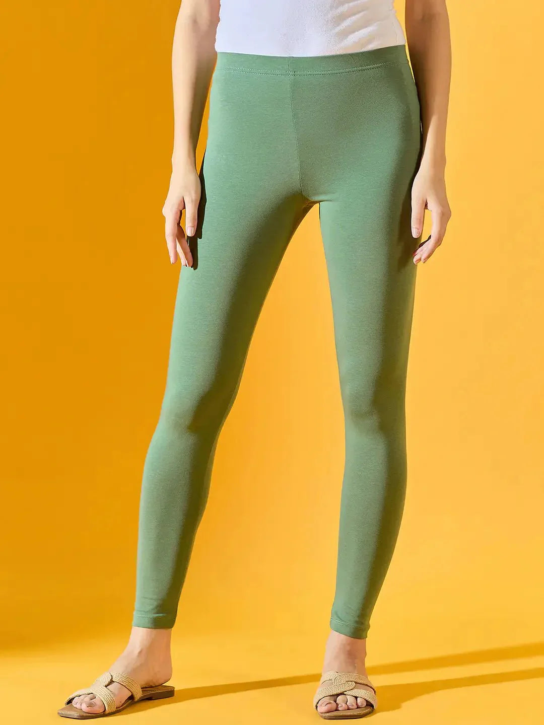 Model in 98degreenorth Women Bright Green Ankle-Length Leggings, white top, and beige sandals against a yellow background.