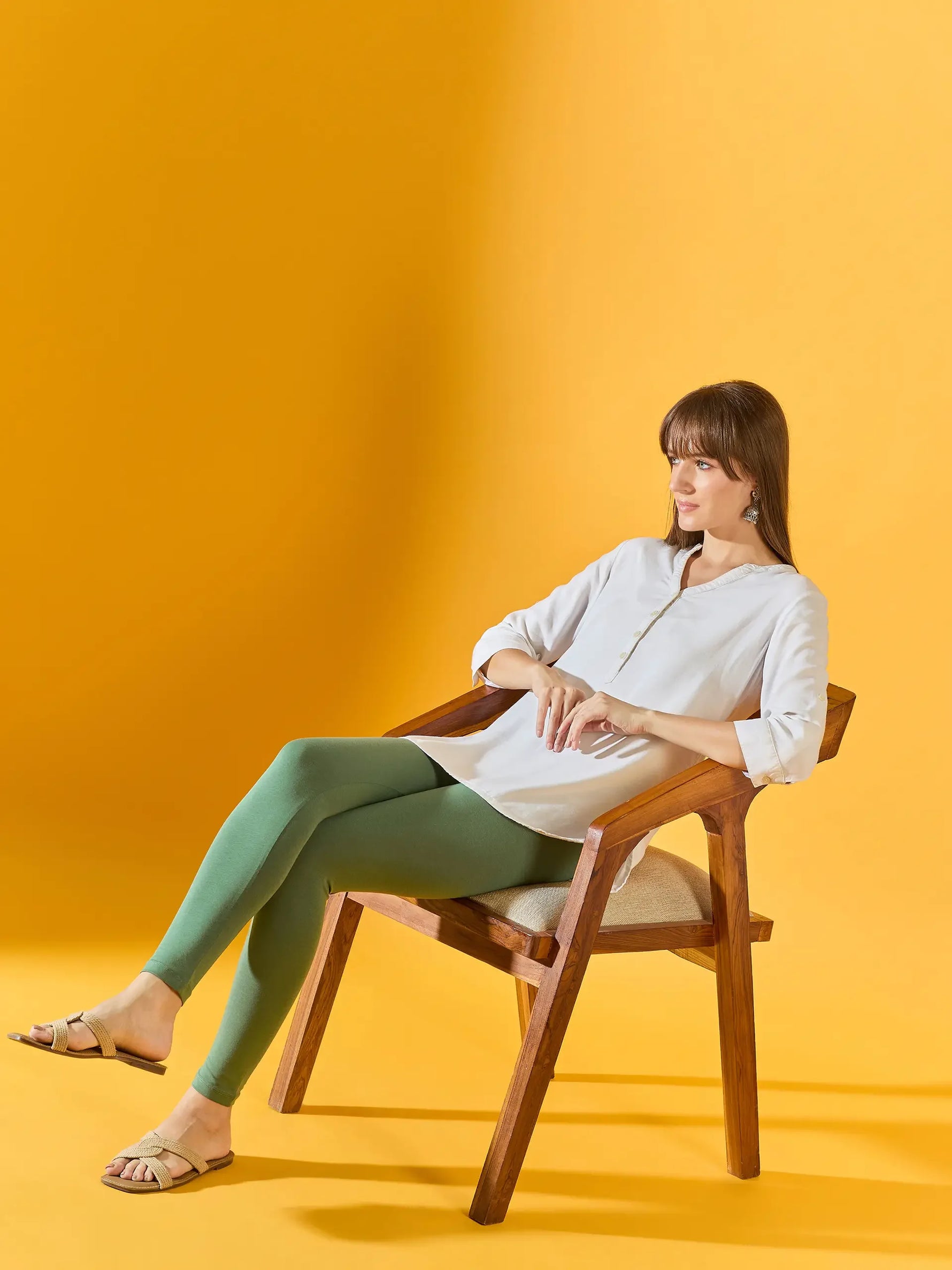 Woman in white top and 98degreenorth Women Bright Green Ankle-Length Leggings relaxes on chair with yellow background.