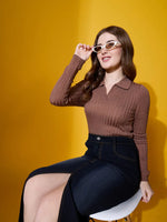 Woman in 98degreenorth camel ribbed collar sweater and dark skirt adjusts white sunglasses against a yellow background.