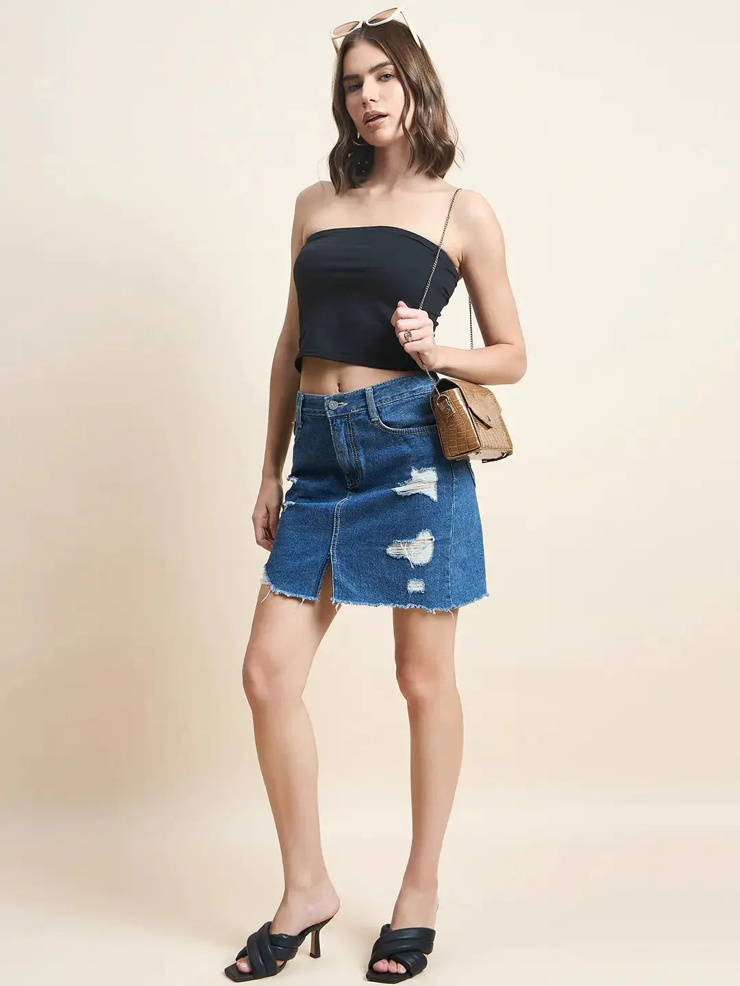 Woman in a 98degreenorth Women Cotton Black Crop Tube Top, distressed denim skirt, black heels, sunglasses, and a brown bag.