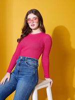 Woman in fuchsia 98degreenorth ribbed sweater and jeans sits on a stool, pink sunglasses, yellow background.