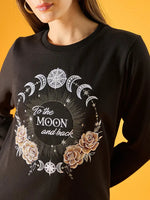 A person wears the 98degreenorth Women Graphic Embroidered Black Round Neck Fleece Sweatshirt, featuring crescent moons, stars, roses, and To the MOON and back text on the front.