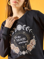 A person wearing a 98degreenorth Women Graphic Embroidered Navy Round Neck Fleece Sweatshirt featuring gold and white moon phases, stars, roses, and To the MOON and back on the front, against a yellow background.