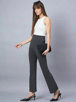 A woman with long straight brown hair and bangs stands against a gray background wearing a sleeveless white top, 98degreenorth Women High-Rise Charcoal Cotton Trousers, black heels, and holding a black clutch.