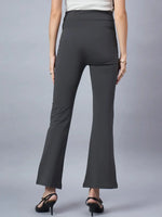 A woman faces away, showcasing 98degreenorth’s Women High-Rise Charcoal Cotton Trousers with a flared silhouette and black heels, paired with a sleeveless light top against a plain gray background.