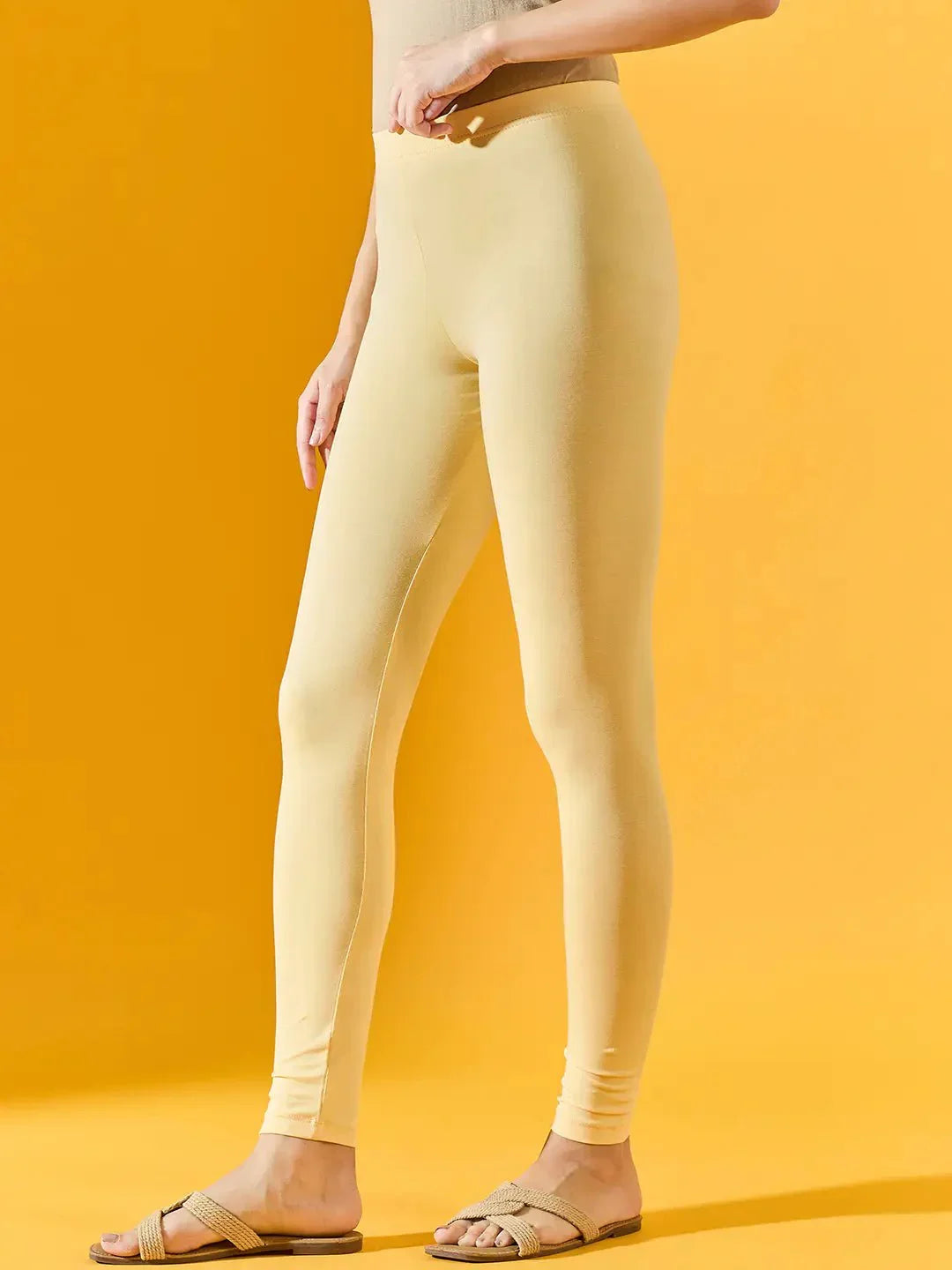 Woman in 98degreenorth Women Lemon Ankle-Length Leggings and beige sandals stands against a yellow background.