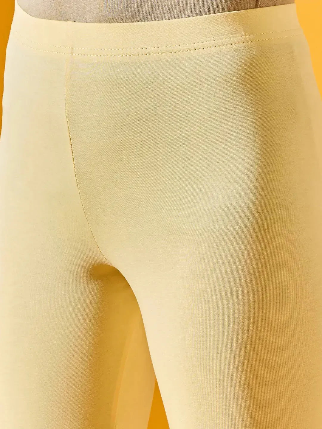 Close-up of a person wearing 98degreenorth Women Lemon Ankle-Length Leggings against a yellow background.