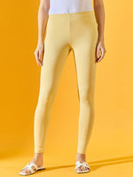 Person in 98degreenorth Women Mango Ankle-Length Leggings, white top, and sandals against a yellow background.