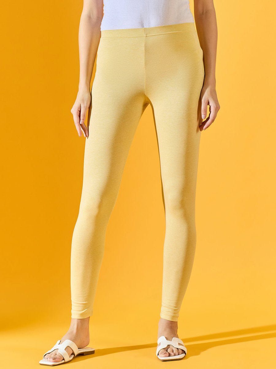 Person in 98degreenorth Women Mango Ankle-Length Leggings, white top, and sandals against a yellow background.