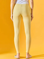 Person in 98degreenorth Women Mango Ankle-Length Leggings and white sandals, back view, against yellow background.