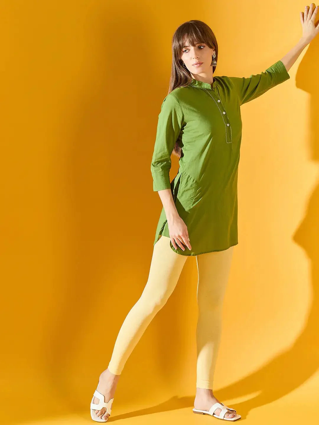 Woman in 98degreenorth Women Mango Ankle-Length Leggings poses by a yellow wall, touching it with one hand.
