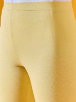 Close-up of a person in 98degreenorth Women Mango Ankle-Length Leggings and a white top against a yellow background.
