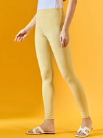 Woman in 98degreenorth Women Mango Ankle-Length Leggings, white sandals, and a white top stands stylishly.