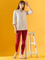 Woman in 98degreenorth Women Maroon Ankle-Length Leggings stands by a white stool against a yellow background.