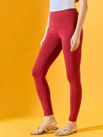 A woman wears 98degreenorth Women Maroon Ankle-Length Leggings, a white top, and sandals against a yellow background.