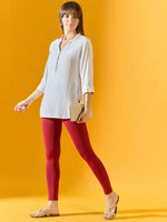 Woman in maroon ankle-length leggings by 98degreenorth holds a beige clutch against a yellow background.