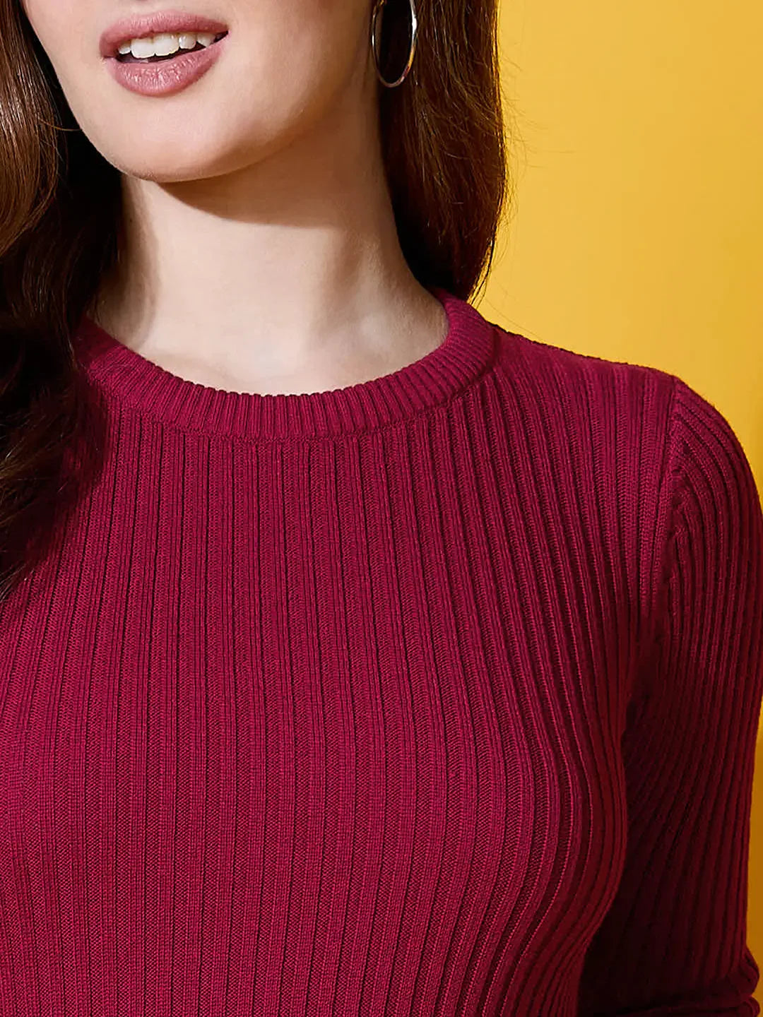 Woman in a 98degreenorth maroon ribbed round neck sweater, styled with hoop earrings against a yellow background.