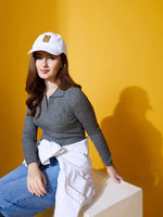 A woman in a 98degreenorth grey ribbed collar sweater and blue jeans sits against a bright yellow background.