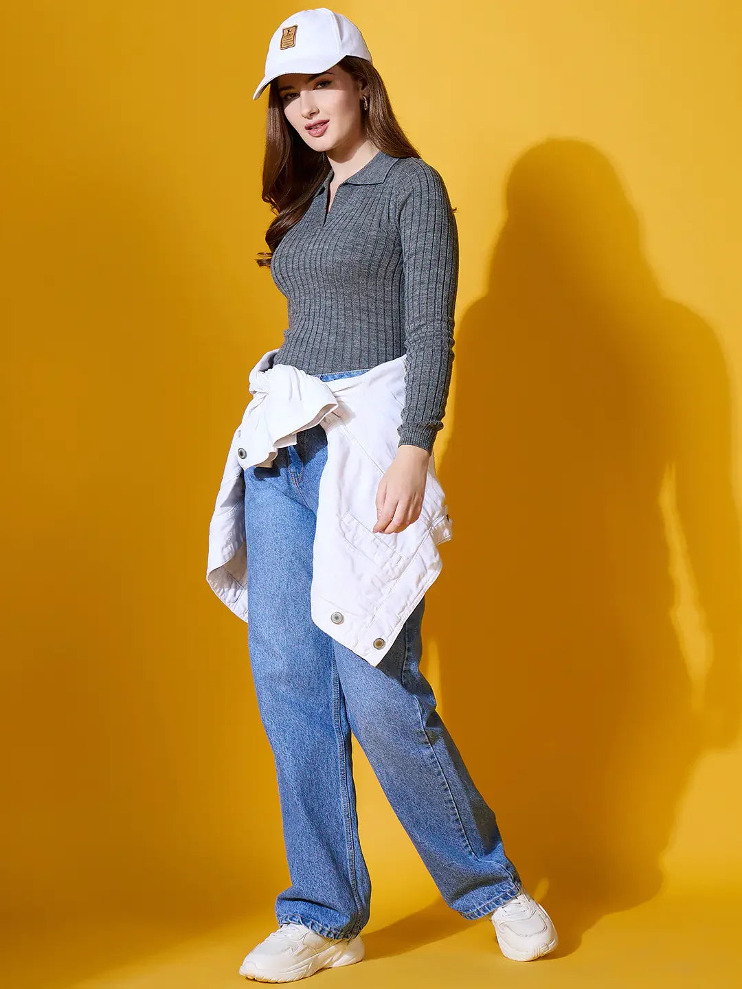 Woman in a 98degreenorth medium grey ribbed collar sweater poses against a yellow background.