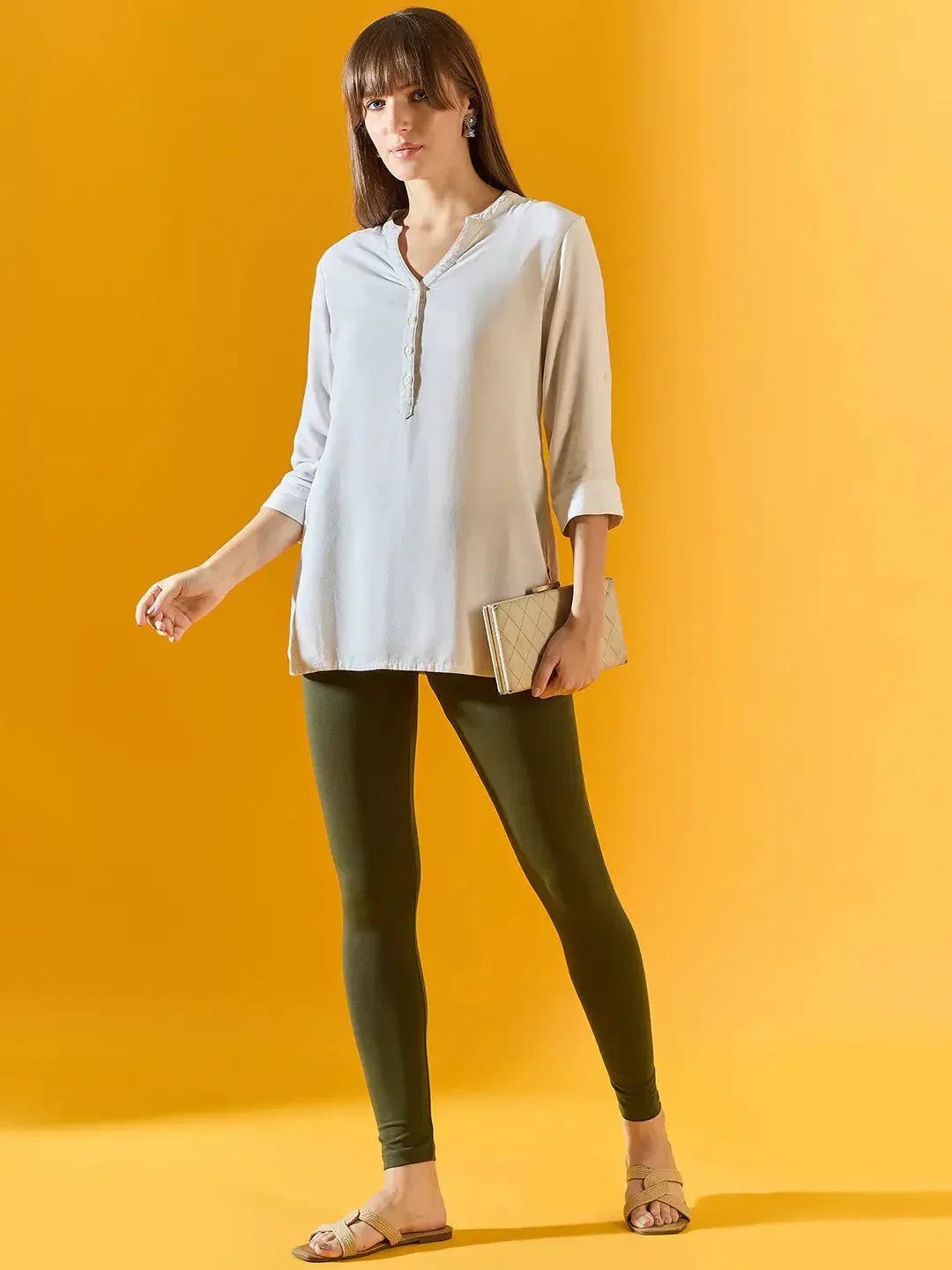 Woman in a light blue top, 98degreenorth Women Olive Ankle-Length Leggings, and sandals holding a clutch.