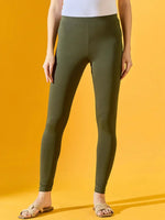 Person wears 98degreenorth Women Olive Ankle-Length Leggings, a white top, and beige sandals before a yellow background.