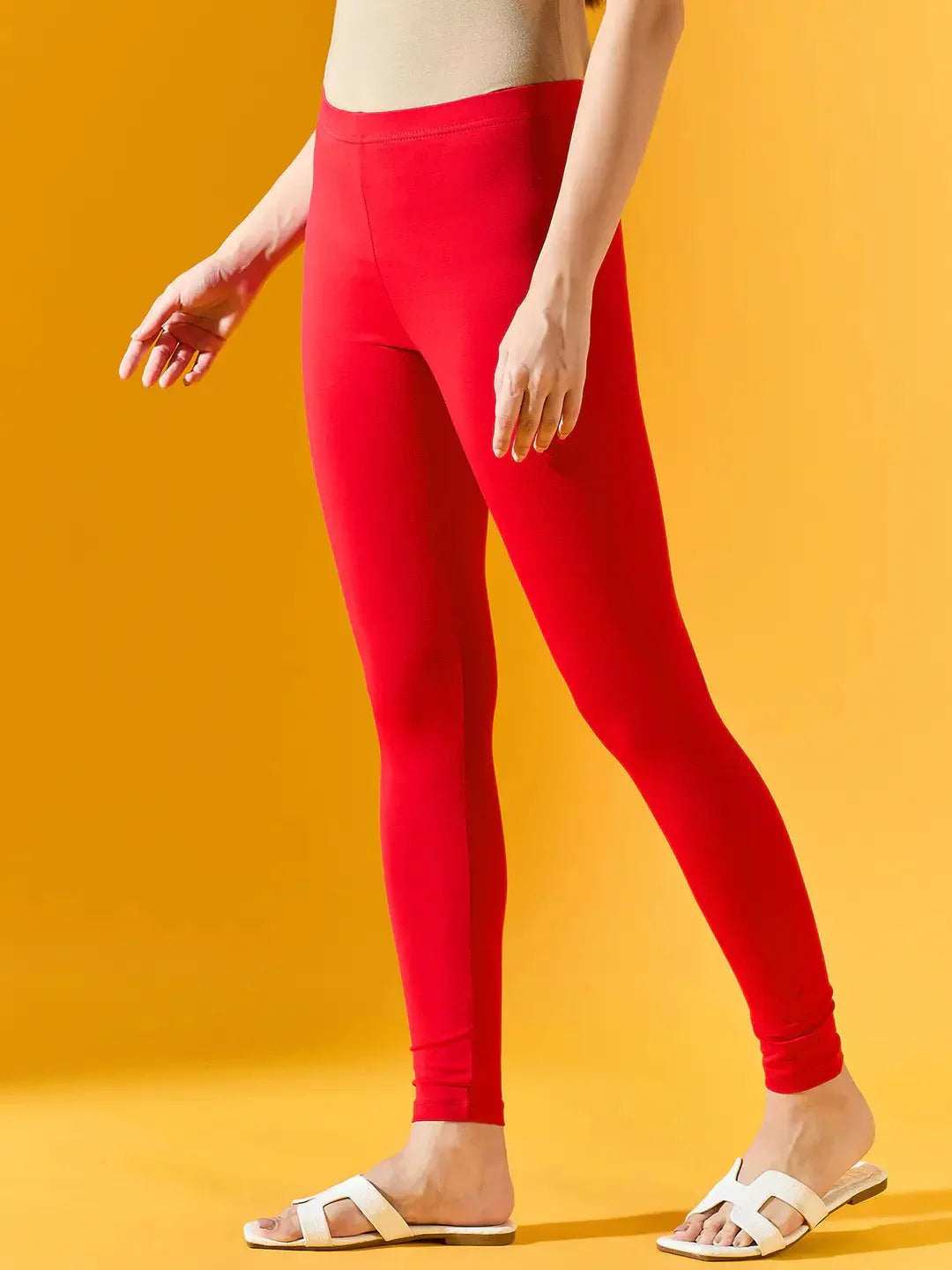A model showcases 98degreenorth Women Red Ankle-Length Leggings with a beige top and white sandals against a bright yellow background, focusing on the trendy lower-body style.