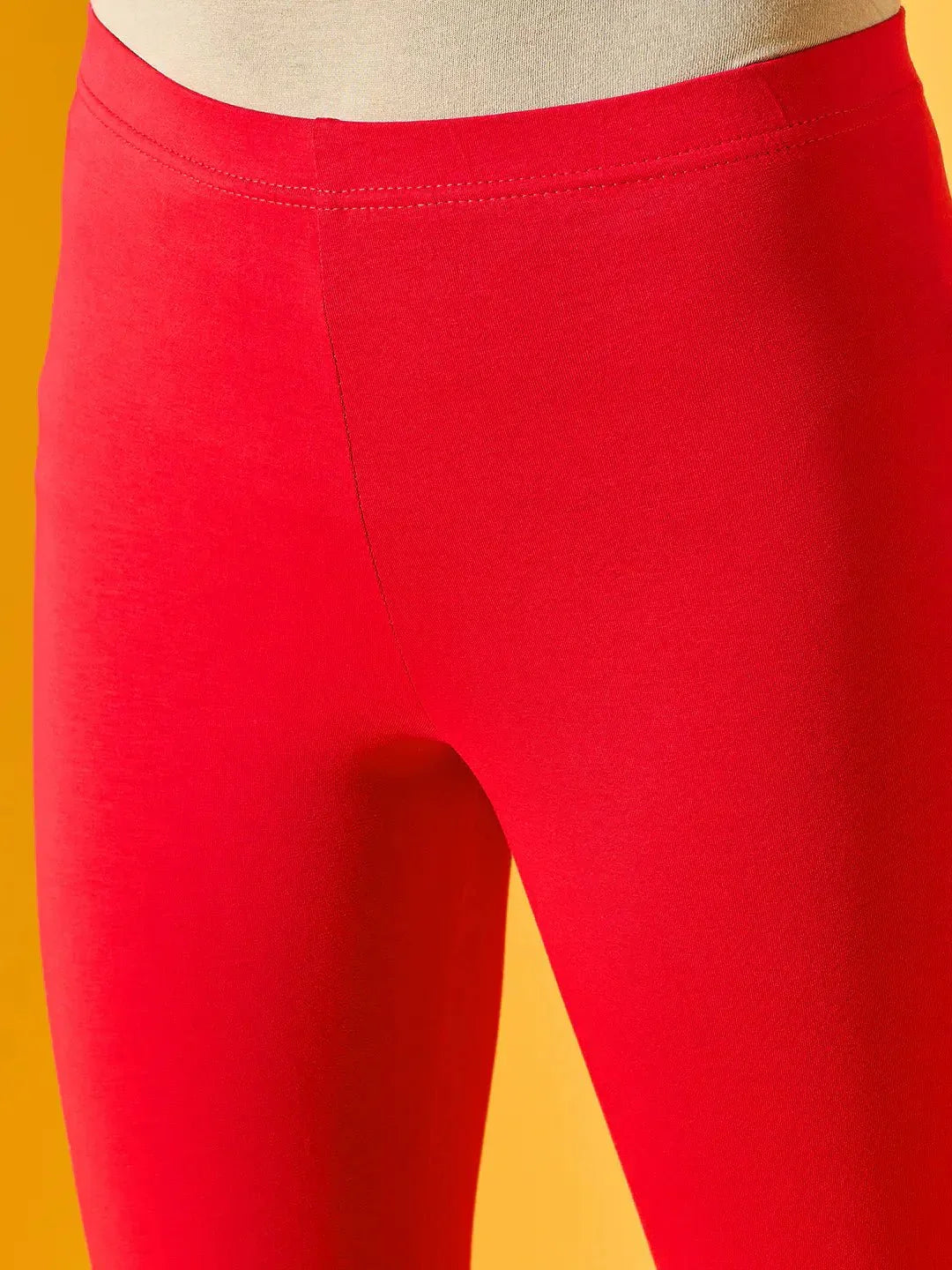 Close-up of a person wearing 98degreenorth Women Red Ankle-Length Leggings, shown from lower torso to upper legs, against a yellow background.