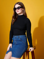 Woman wears 98degreenorth Ribbed High Neck Sweater – Black, seated on stool with yellow background.