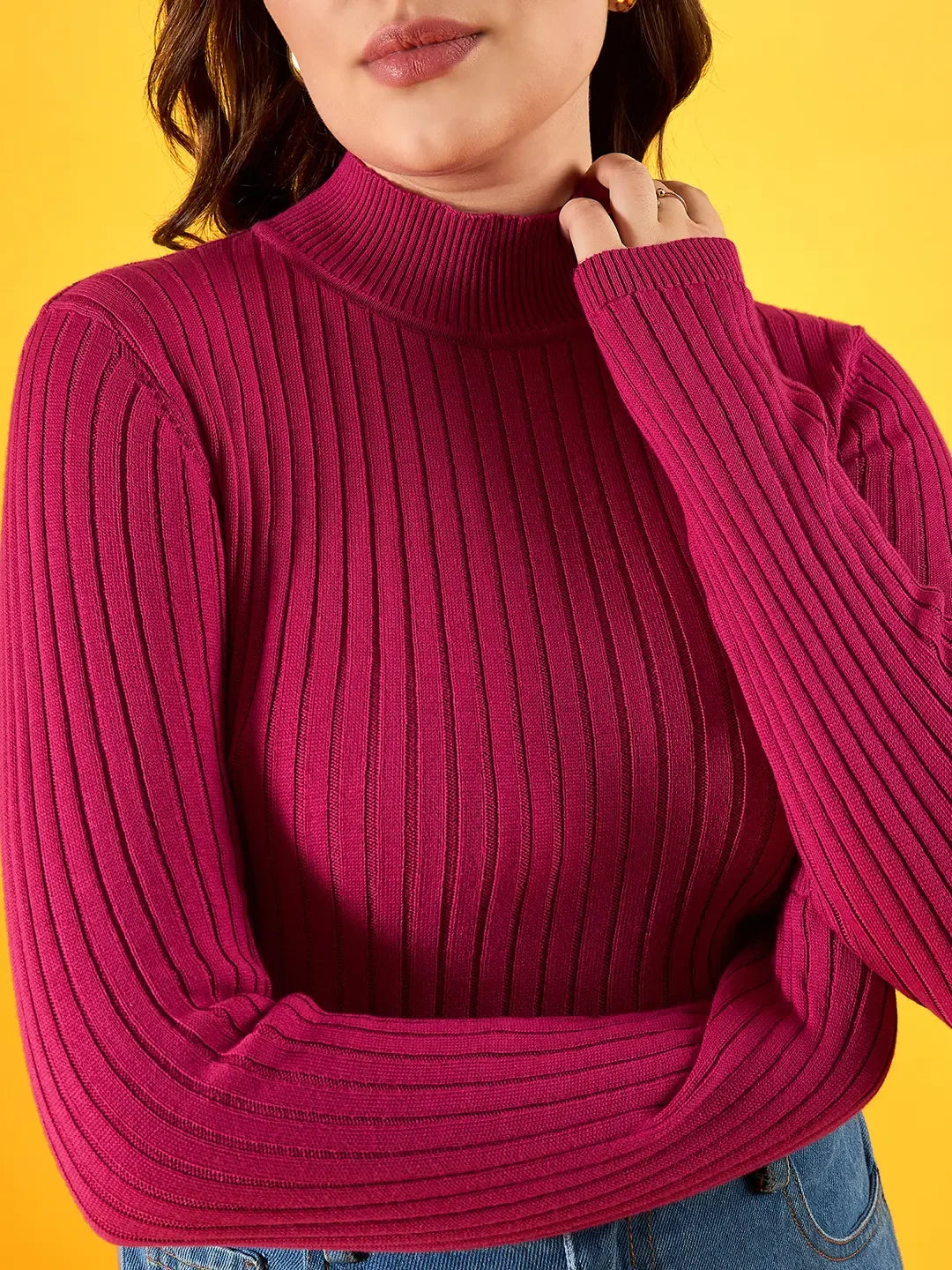 A woman in a 98degreenorth fuchsia ribbed high neck sweater stands against a vibrant yellow background.