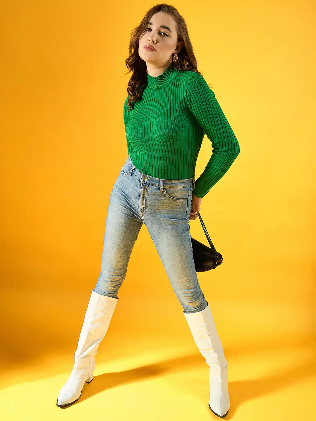 Woman models 98degreenorth Women Ribbed High Neck Sweater – Green, paired with light blue jeans and white boots.
