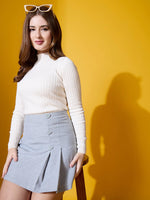 Woman in 98degreenorth’s off-white ribbed high neck sweater sits on a stool, sunglasses on head, yellow background.