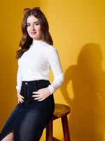 A woman wears a 98degreenorth ribbed high neck white sweater, seated before a vibrant yellow background.