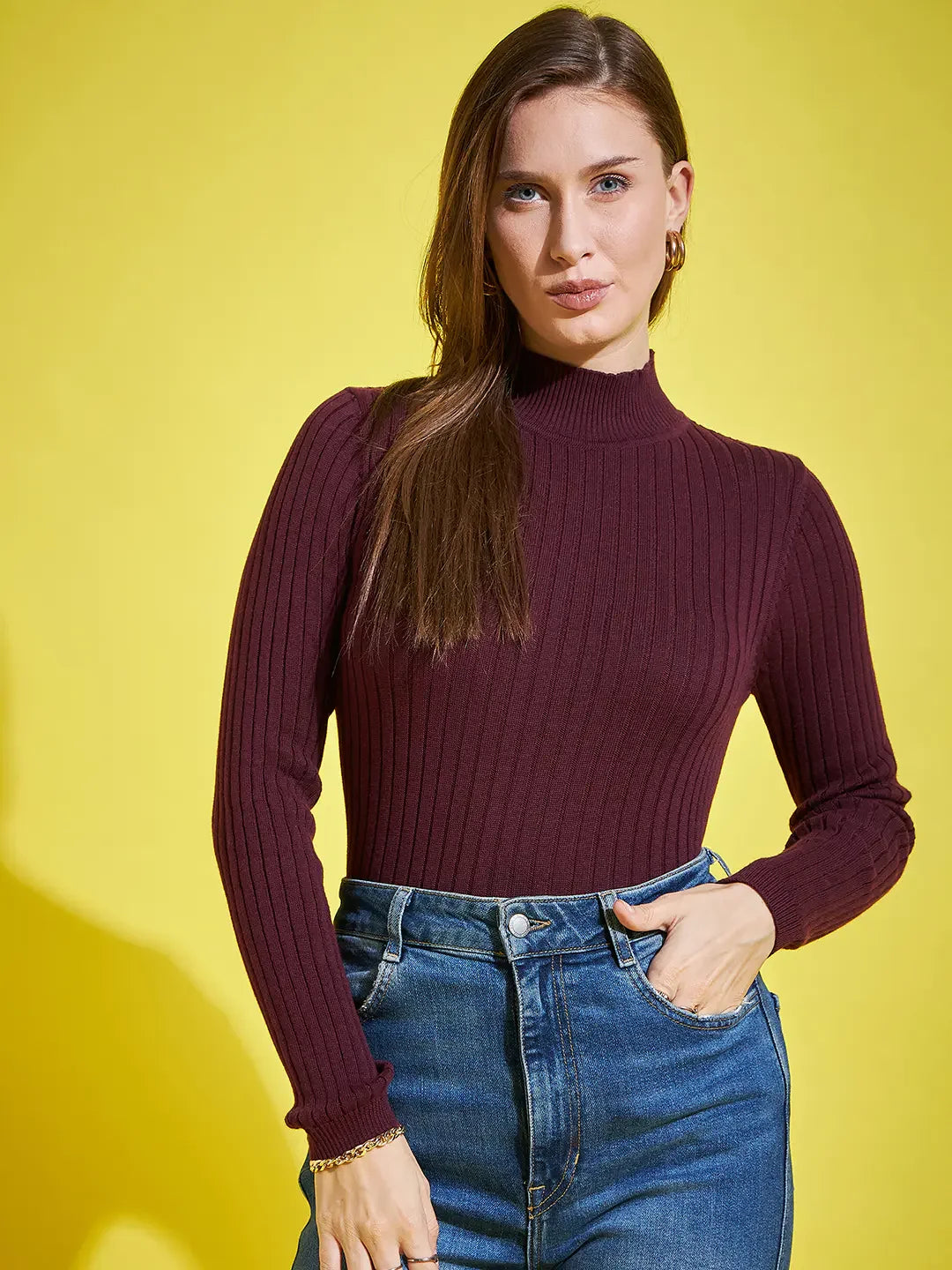 Woman in 98degreenorth’s wine ribbed high neck sweater stands against a yellow background, looking at the camera.