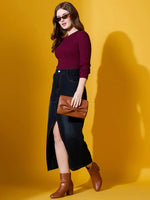 Woman in 98degreenorth Rosewood Ribbed Sweater, dark denim skirt, brown boots—chic winter style on yellow.