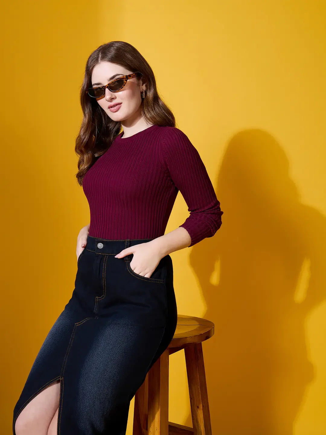 Woman in rosewood ribbed sweater by 98degreenorth poses stylishly, pairing winterwear with flair against a yellow backdrop.