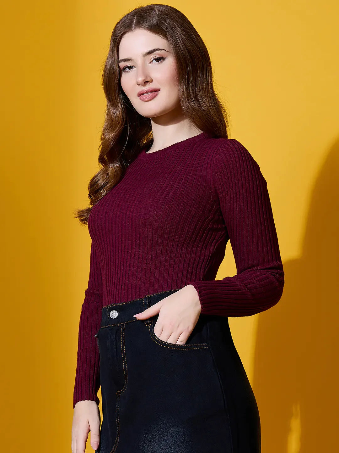 Woman with long brown hair wears the 98degreenorth Rosewood Ribbed Sweater, standing against a yellow background.