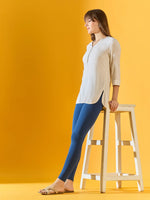 Woman in a white tunic and 98degreenorth Women Teal Blue Ankle-Length Leggings leans on a tall stool.