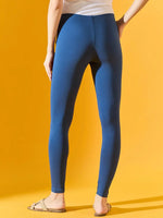 A woman in 98degreenorth Women Teal Blue Ankle-Length Leggings, a white top, and sandals stands by a yellow background.