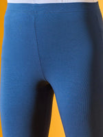 Close-up of a person wearing 98degreenorth Women Teal Blue Ankle-Length Leggings against a yellow background.