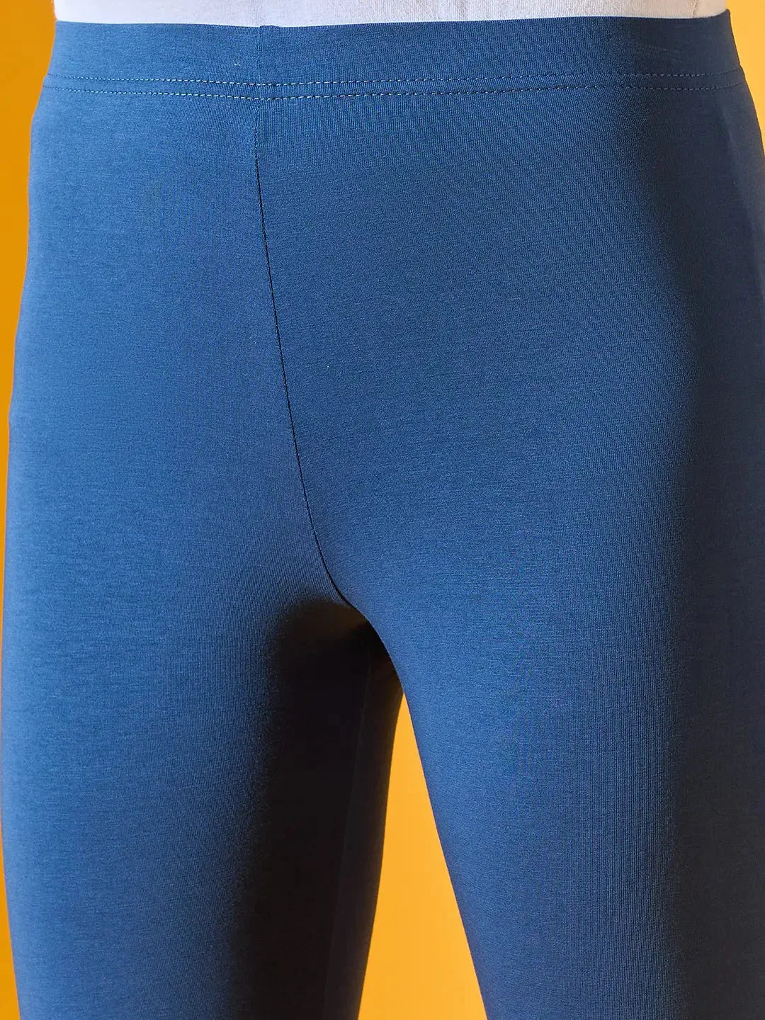 Close-up of a person wearing 98degreenorth Women Teal Blue Ankle-Length Leggings against a yellow background.